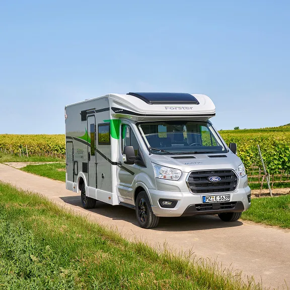 Wohnmobil in weiter Landschaft mit Regenbogen im Hintergrund.